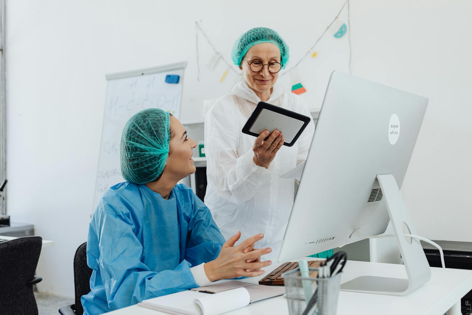 Two female medical researchers discussing a project using a tablet in a laboratory setting.